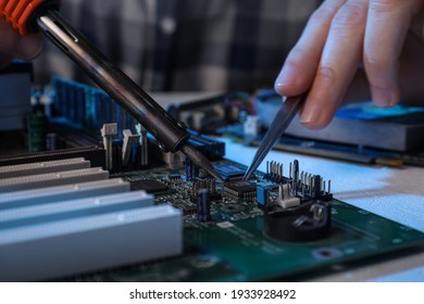 Technician repairing electronic circuit board with soldering iron at table, closeup
