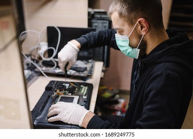 Technician repairing a laptop in the lab. Concept of repair computer, electronic, upgrade, technology.  Coronavirus. Man working, wearing protective mask in workshop.