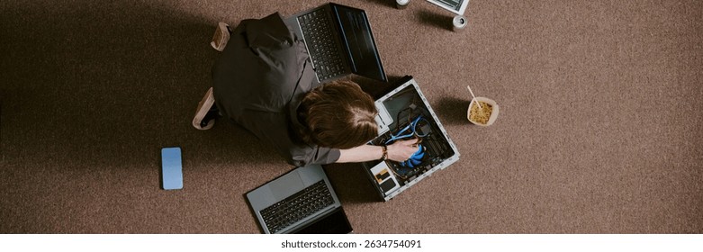 Technician repairing multiple laptops while sitting on carpeted floor, using various tools and devices, showing in depth focus and technical skillset during task