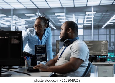 Technician requesting help from manager while working on computer in data center, monitoring hardware energy consumption. Team leader overseeing IT specialist checking for system failures