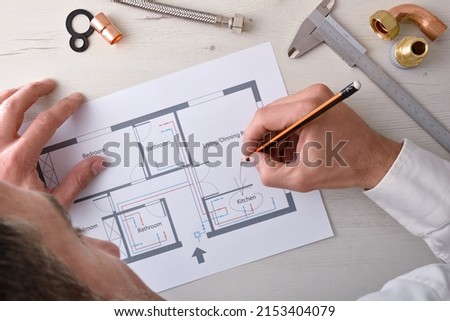 Technician reviewing the design of a home water installation on his office table with materials around. Top view. Horizontal composition.