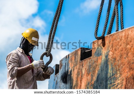 Technician rigger checking crane hook sling safety before lifting heavy steel product outside the factory.