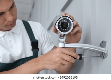 Technician with screwdriver installing CCTV camera on wall indoors
