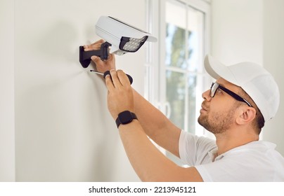 Technician With Screwdriver And Smart Glasses Installs Security Remote Camera With LED Light On Wall In White Office Or Medical Clinic. Security And Privacy Round The Clock Control.