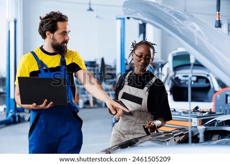 Technician servicing broken vehicle, checking for faulty brakes under manager supervision. Smiling repairmen in auto repair shop working together on fixing automobile, discussing best options