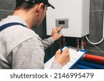 Technician servicing holding clipboard and inspecting heating system in boiler room