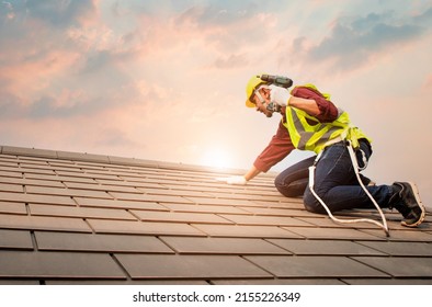 Technician in shirt and jeans wear helmet safety suithand use screwdriver tool install repair C-Pack roof on high work place.Workers work at heights with full safety suits on construction sites. - Shutterstock ID 2155226349