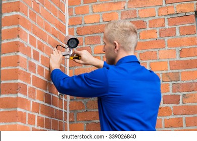 Technician Standing On Ladder Installing Camera On Wall