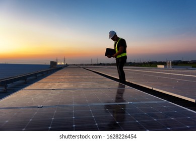 Technician Standing On Roof Checking Photovoltaic Cells Panels On Factory, Maintenance Of The Solar Panels, Engineer Service, Inspector Concept. Silhouette Photo.