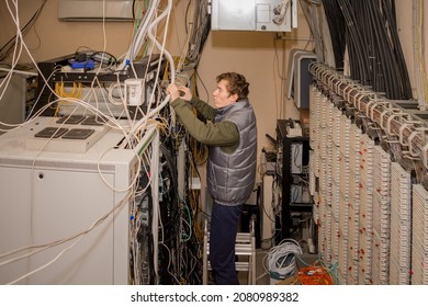 A Technician Is Standing On The Stairs And Laying Wires In The Server Room. Maintenance Of Computer Equipment In The Old Data Center. The Man Works Near The Server Racks.