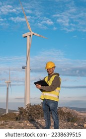Technician supervising, pointing on the folder with cheerful expression, at the wind farm. - Shutterstock ID 2238639515