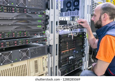 Technician Switches  Cable Of Routers. Specialist Connects  Wires In The Server Room Of Data Center. Man Works With Telecommunications. Guy Is Sitting Near  Racks With  Computer Equipment.