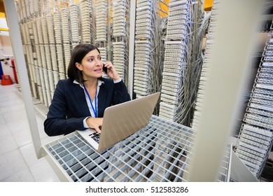 Technician talking on mobile phone while using laptop in server room - Powered by Shutterstock