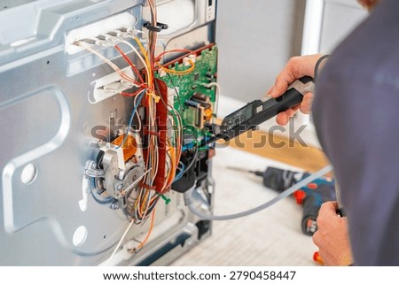 Technician testing electronic components and wiring inside disassembled electric oven. Appliance diagnostics and professional repair service concept