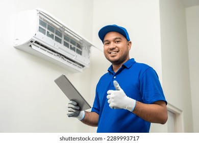 Technician in uniform using tablet to check list of maintenance and cleaning filters of air conditioner. Air condition maintenance service. Home services concept.
