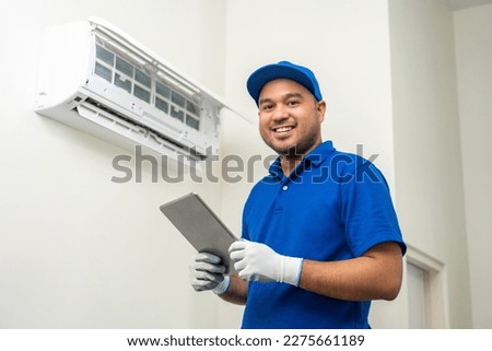 Technician in uniform using tablet to check list of maintenance and cleaning filters of air conditioner. Air condition maintenance service. Home services concept.