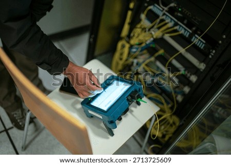 A technician uses a testing device to analyze network performance in a server room. The image captures the essential tools and technology for diagnosis.