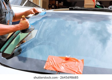 Technician uses tools to replace cracked windshield at car repair facility during work day.