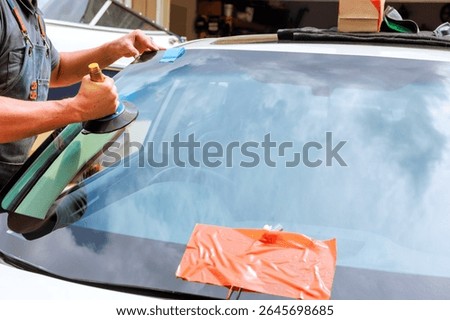 Technician uses tools to replace cracked windshield at car repair facility during work day.