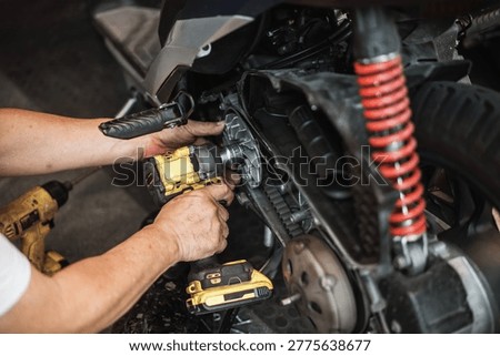 technician using a cordless impact driver to disassemble or assemble motorcycle engine parts. Professional maintenance of a scooter's belt drive system in a garage workshop.