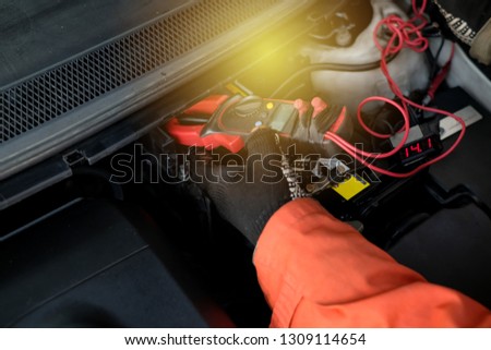 Technician using digital clamp meter to measure and check car battery voltage after changing.