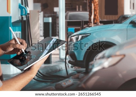 Technician using digital tablet for diagnostics and data analysis while an electric vehicle charges at a modern EV charging station. Concept of smart maintenance, clean energy, automotive technology.