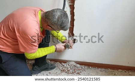A technician is using a hammer to drill into a cement wall to shore up electrical wires.