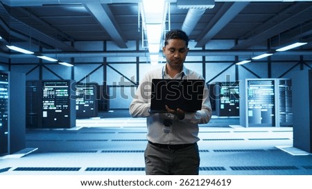 Technician using laptop in data center, managing servers, operating systems. Professional in server hub using notebook to ensure networks are secure and functioning properly, camera B