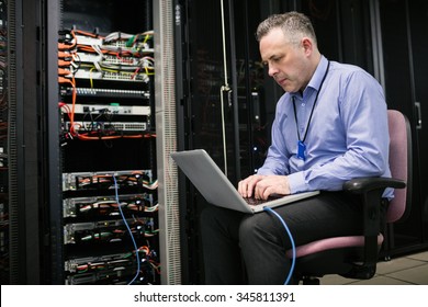 Technician Using Laptop In Server Room At The Data Centre