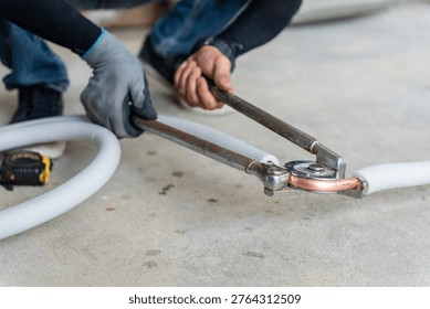 Technician using manual pipe bender tool to bend copper pipe for air conditioning installation, Close up of professional worker hands bending copper tube with insulation for hvac system