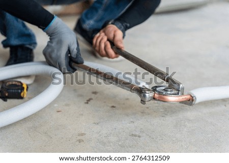 Technician using manual pipe bender tool to bend copper pipe for air conditioning installation, Close up of professional worker hands bending copper tube with insulation for hvac system