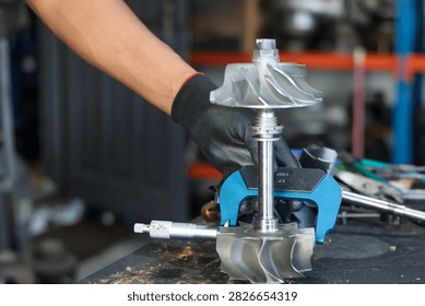 Technician using a micrometer tool to precisely measure a turbocharger shaft assembly in an automotive workshop.
