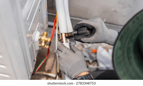 Technician using pipe cutter on copper tubing for air conditioner installation, Hvac repairman cutting copper pipe of an air conditioning system, Hands using tube cutter on ac unit refrigerant line
