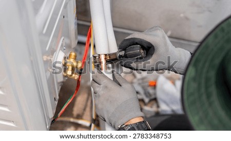 Technician using pipe cutter on copper tubing for air conditioner installation, Hvac repairman cutting copper pipe of an air conditioning system, Hands using tube cutter on ac unit refrigerant line
