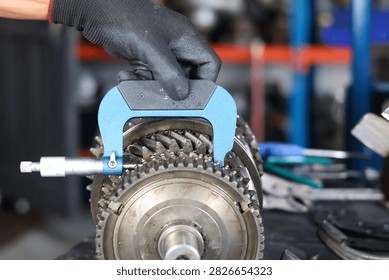 Technician using a precision micrometer tool to measure a manual transmission synchronizer gear in an automotive workshop.
