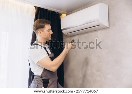 Technician is using a remote control to operate a modern wall mounted air conditioning unit, ensuring optimal cooling performance