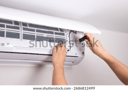 Technician using screwdriver to fix air conditioning unit. Concept of electrical repair, air conditioner service, HVAC maintenance.