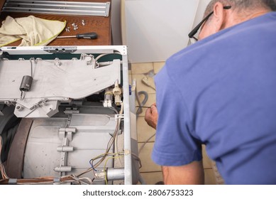 Technician using a screwdriver to fix a broken washing machine, performing maintenance work on the internal components of the home appliance