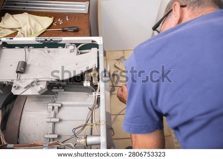 Technician using a screwdriver to fix a broken washing machine, performing maintenance work on the internal components of the home appliance