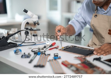Technician using screwdriver fixing tablet computer motherboard in electronics repair shop