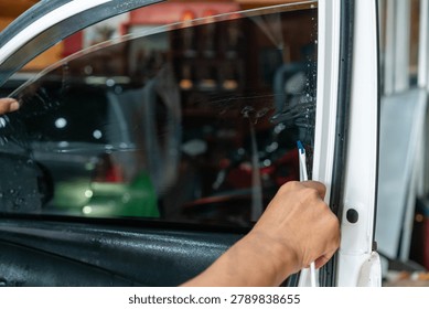 A technician using a specialized tool to smooth and apply dark window tint film onto a car door window during installation process.