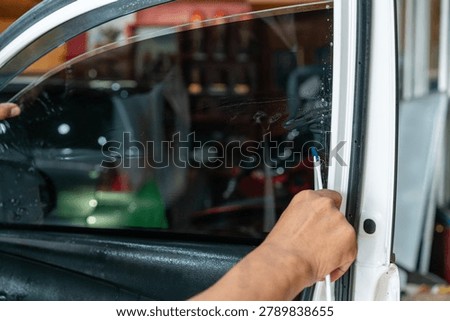 A technician using a specialized tool to smooth and apply dark window tint film onto a car door window during installation process.