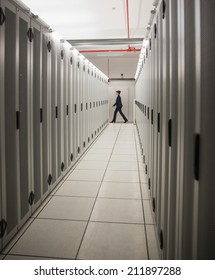 Technician Walking In Server Hallway In Large Data Center