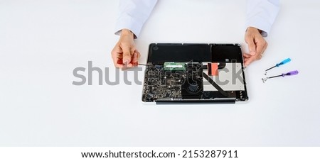An IT technician in white robe is repairing a broken notebook laptop computer full of dust on white background. Computer service concept copy space .
