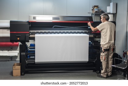 Technician worker operator works on large premium industrial printer and plotter machine in digital printshop office - Shutterstock ID 2052772013