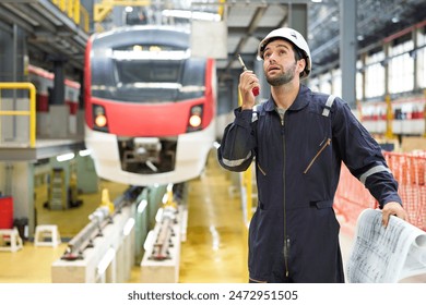 Technician or worker talking about work on walkie talkie and holding blueprint paper at construction train station