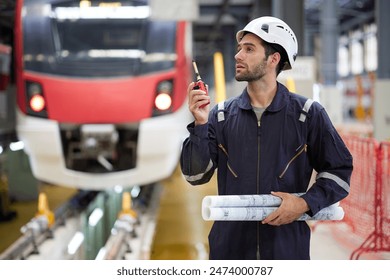 Technician or worker talking about work on walkie talkie and holding blueprint paper at construction train station