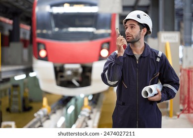 Technician or worker talking about work on walkie talkie and holding blueprint paper at construction train station