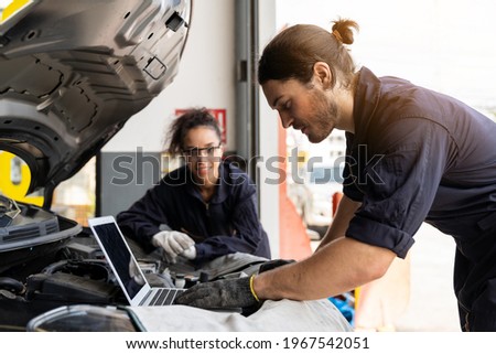 Technician worker working and using laptop computer maintenance car engine under hood of car at auto car repair service. Group of mechanic vehicle service maintenance under car condition in the garage