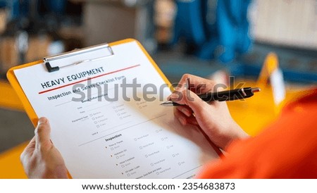 A technician worker is writing on heavy equipment inspection checklist before repairing the machinery in manufacturing factory (as blurred background). Industrial working action. 